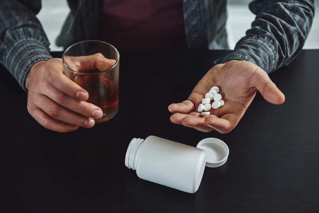 Person holding Tylenol® and a glass of alcohol, illustrating danger