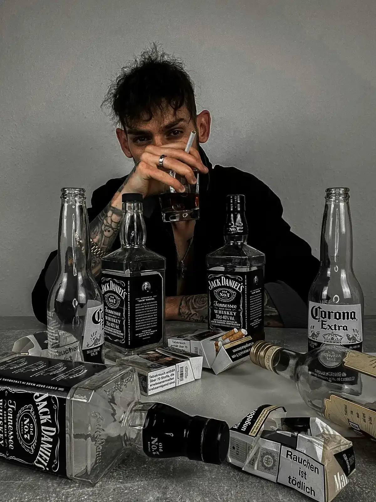 Man with wet brain syndrome sitting at a table full of empty whiskey bottles