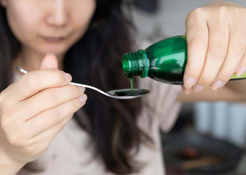 Woman about to take a tablespoon of cough drops