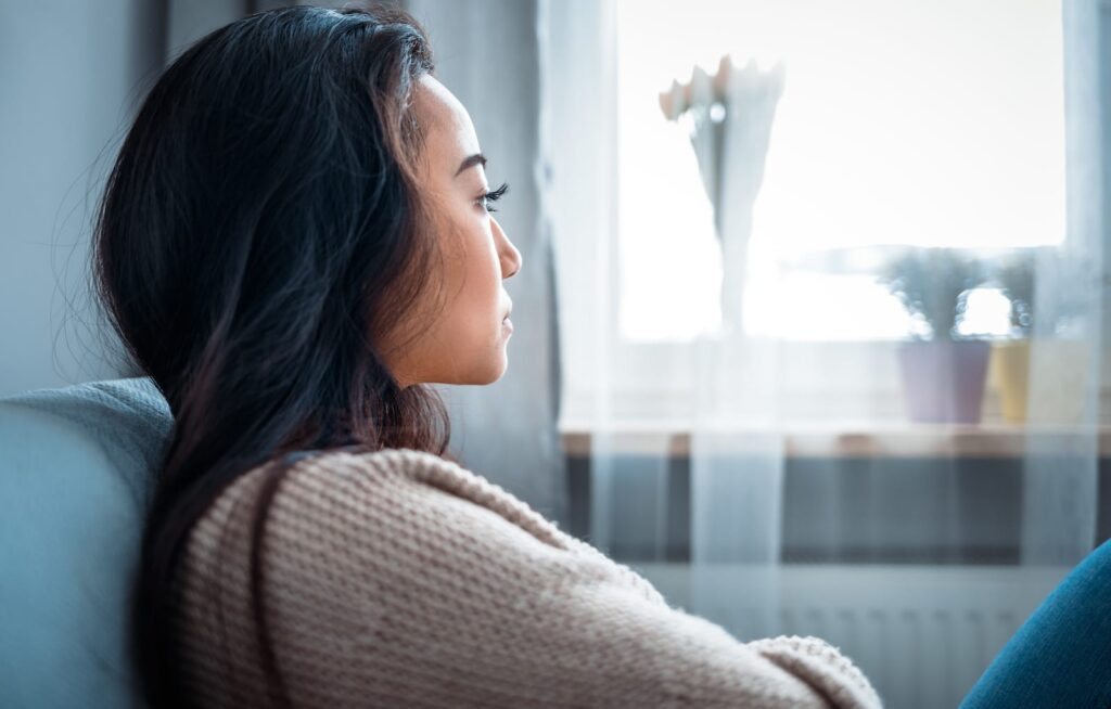 Person sitting on a couch, looking out a window, reflecting on prednisone withdrawal and the importance of medical supervision during tapering.