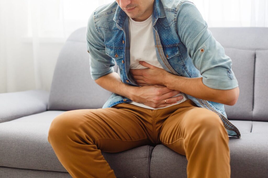 Man sitting on a couch, holding his stomach in discomfort, illustrating the physical symptoms associated with Xanax withdrawal.