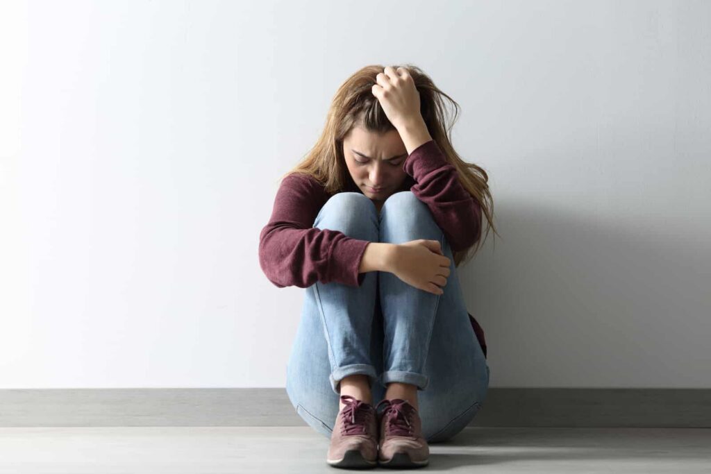 Person sitting on the floor with knees drawn up, looking distressed, reflecting the emotional struggles associated with cocaine comedown and withdrawal symptoms.