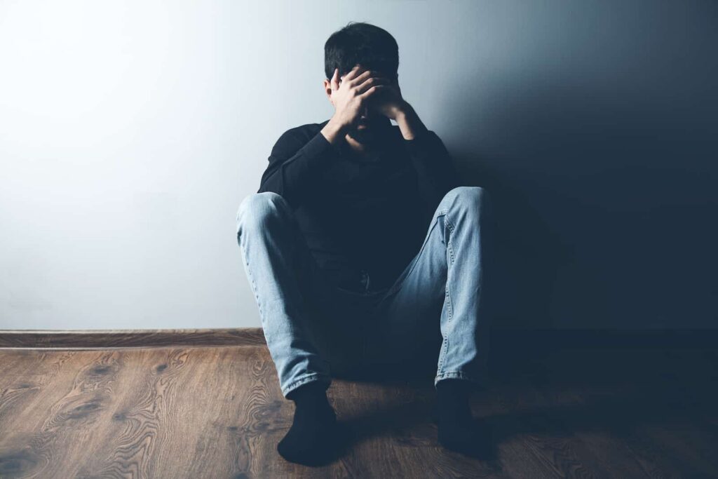 Person sitting on the floor with head in hands, expressing distress, reflecting the emotional struggles associated with painkiller addiction and withdrawal symptoms.