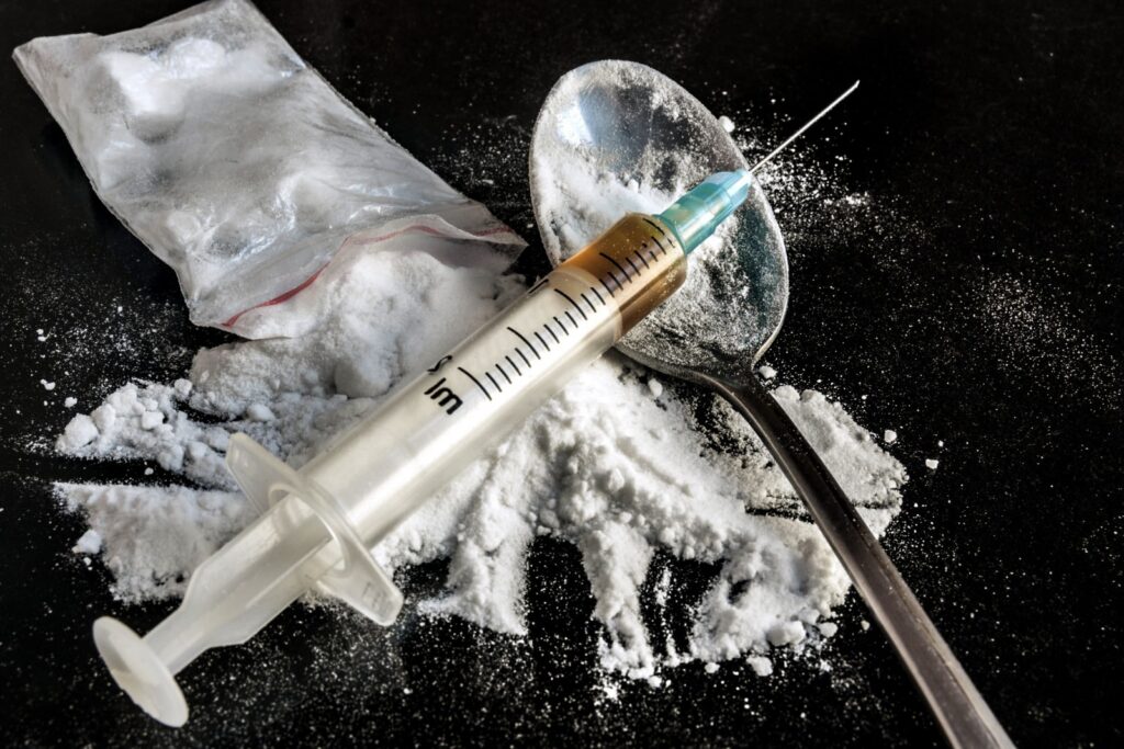 Syringe, spoon, and heroin powder on a dark surface, illustrating the dangerous aspects of heroin use and addiction.