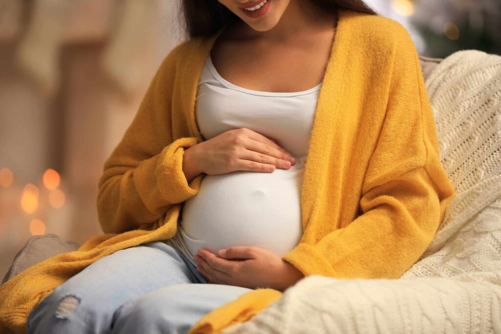 Pregnant woman gently cradling her belly, wearing a cozy yellow cardigan, symbolizing comfort and care during pregnancy.