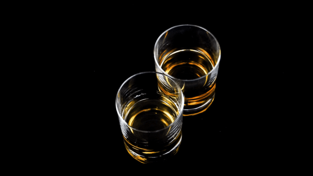 Two glasses of amber liquid on a black background, representing alcohol, highlighting the risks of mixing stimulants like Adderall and modafinil with alcohol.