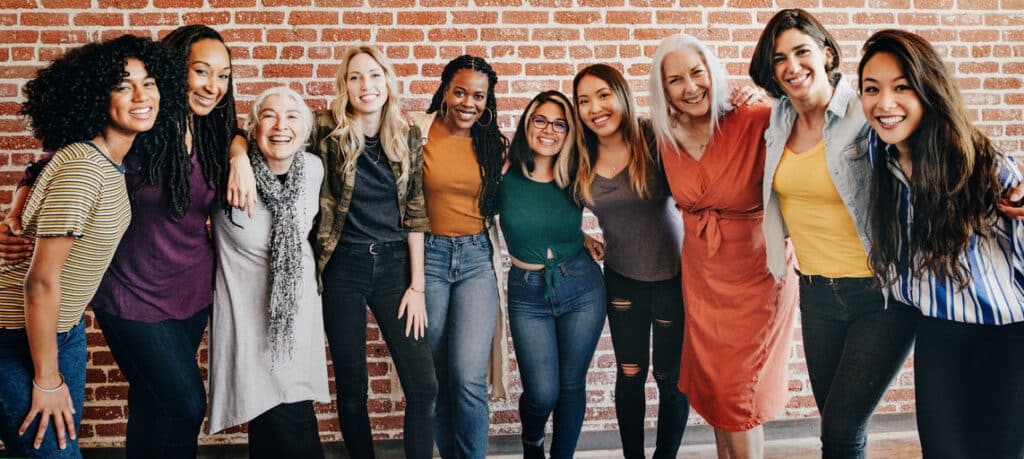 Group of diverse women smiling and posing together in a supportive environment, symbolizing friendship and community in recovery.