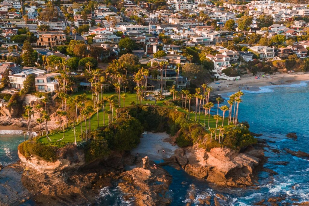 Coastal view of a palm-lined beach area in Orange County, featuring residential homes, rocky shoreline, and clear blue water, emphasizing the natural beauty and community environment relevant to local addiction recovery support.