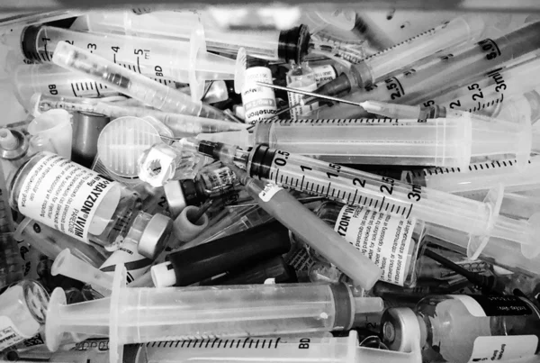 Black and white photo of syringes and pill bottles of addictive drugs