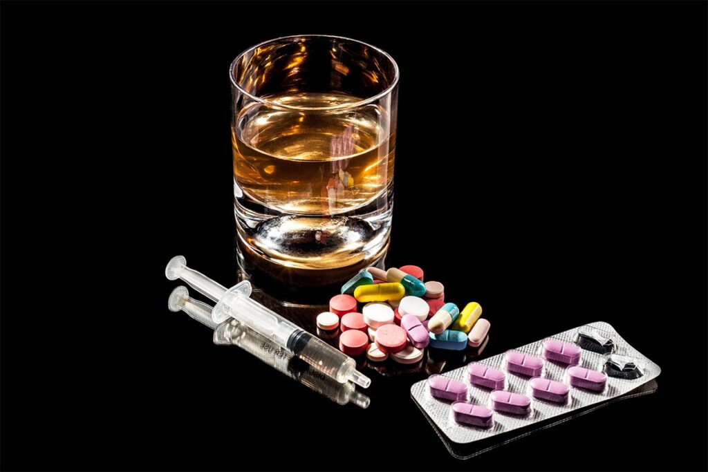 Alcohol and steroid pills with syringes, illustrating dangers of combining substances.