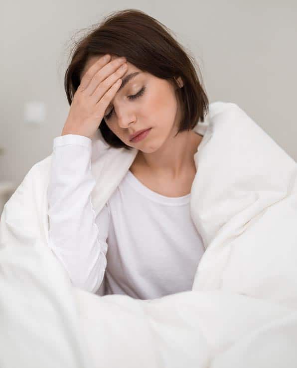 Woman experiencing fentanyl withdrawal symptoms, head in hand, wrapped in a blanket.