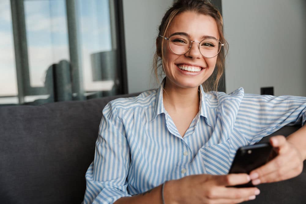 Smiling woman with glasses looking at phone, representing addiction recovery support.